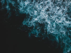 從空中俯瞰海浪破碎，白色泡沫與黑暗海水形成對比。