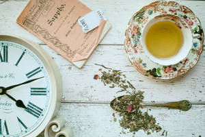 復古時鐘、茶杯和茶葉在質樸的木質表面上。