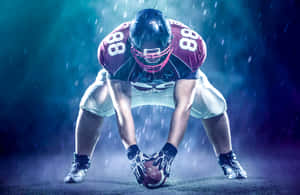 身穿栗色球衣的足球員在雨中，於藍色舞台燈光下蹲著抱住球。 — NFL 美式足球 GIF 壁紙