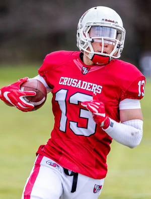 身穿紅色 Crusaders 球衣的足球員在草地上帶球奔跑。