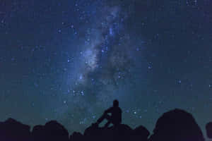 人在星空下坐在岩石上，銀河可見 — 星星 壁紙