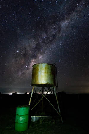 生鏽的水塔和綠色桶子在星空夜空下，有銀河