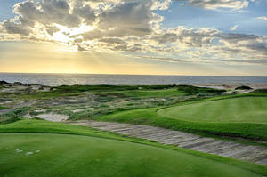 日落時分的沿海高爾夫球場，綠色球道和海景。
