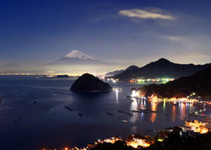 夜晚的富士山，發光的沿海城鎮和星空倒映在平靜的水面上。