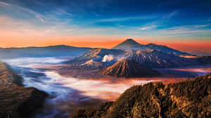 日出時分的火山山脈，薄霧流過山谷，山峰在溫暖的橙色和涼爽的藍色調中閃耀。