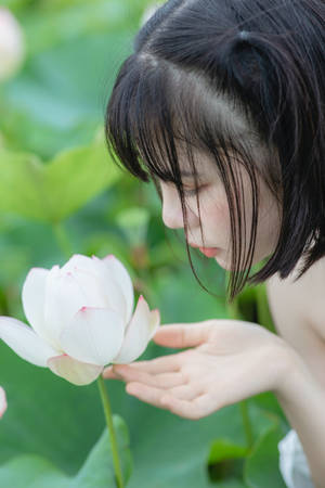 年輕女性在綠色池塘中溫柔地觸摸一朵白色蓮花。