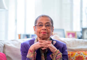 身穿紫色西裝外套的老年女性在室內梳化上雙手交握而坐