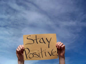 手舉著寫有Stay Positive的標語，背景是藍天。