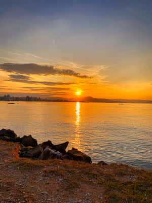 夕陽映照水面，城市天際線與遠山為背景。