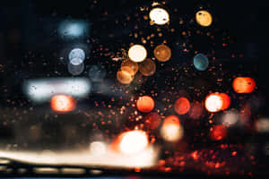 汽車擋風玻璃上的雨點將城市燈光模糊成彩色散景，在夜晚。