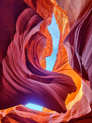 狹縫峽谷的彎曲紅色、橙色和紫色砂岩牆壁，上方可見藍天。
