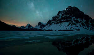 在繁星點點的夜空下，積雪的山峰倒映在湖中，銀河清晰可見。 — 湖景 壁紙