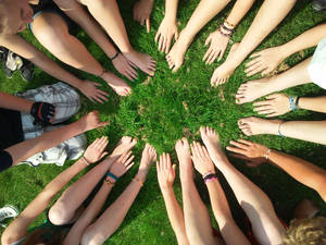 Group of young people sitting in a circle on grass with hands and feet touching.