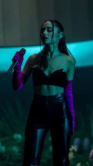 歌手 Ariana Grande 在藍色燈光下穿著黑色服裝和紫色手套在舞台上表演。 — 山邊 壁紙