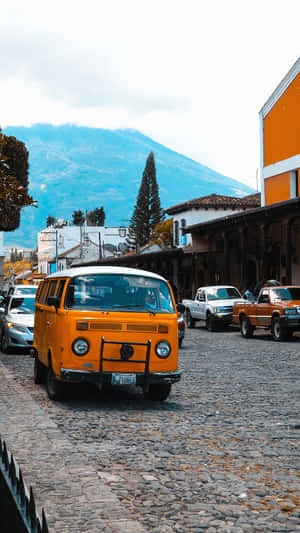 復古橙色貨車停在鵝卵石街道上，背景有山。 — 70年代gif 壁紙