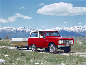 一輛紅色1966年福特Bronco，車內有家人，穿過草地，背後是積雪的山脈。