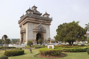 公園中的歷史石拱門，配有修剪整齊的樹籬和樹木 — 建築 壁紙