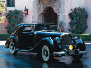 黑色 vintage Bentley 停在宏偉豪宅前，濕潤路面映出倒影。