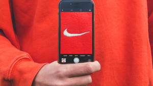 手拿著手機拍攝紅色布料上的Nike標誌。