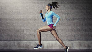 運動型女性身穿藍色上衣和洋紅色短褲，在磚牆前奔跑。 — 型格 Nike 壁紙