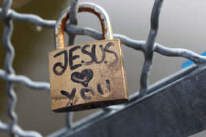 一個青銅掛鎖，上面寫著「JESUS ❤️ YOU」，掛在鐵絲網圍欄上。