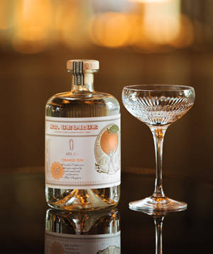 深色表面上的 St George Atlas Orange Gin 酒瓶和 coupe 杯，帶有溫暖燈光。