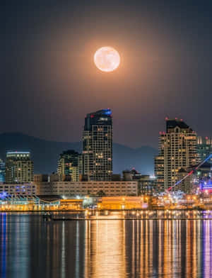 夜晚城市上空的滿月，燈光在水面上反射。