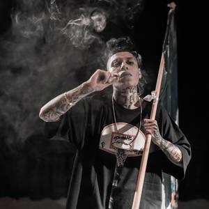 有紋身的男人抽煙，在煙霧瀰漫的黑暗環境中拿著旗幟和籃球框吊飾。