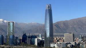 現代玻璃摩天大樓聳立於城市之上，遠處有白雪覆蓋的山峰。