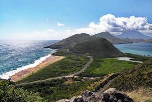 海岸公路蜿蜒穿過綠色山丘，旁邊是沙灘和碧綠色的海洋。 — 島嶼 壁紙