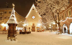 夜晚的雪景小鎮廣場，燈光璀璨的建築和節日燈飾。