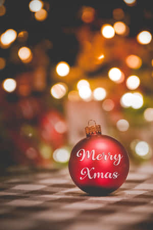 一個紅色聖誕裝飾，上面有白色草書文字寫著Merry Xmas，放在格仔表面上，背後有模糊的燈光。 — 小米Pad 7 Ultra 壁紙
