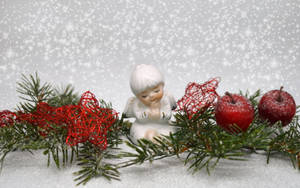 白色天使雕像被松樹枝、紅心和雪覆蓋的蘋果包圍。