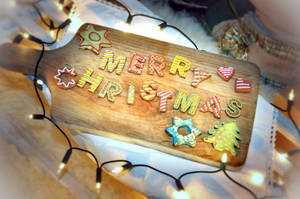 薑餅曲奇在木板上拼出 Merry Christmas，配有燈串。 — 聖誕快樂 GIF 壁紙