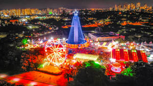 夜晚的節日遊樂園，背景是發光的遊樂設施和城市燈光。