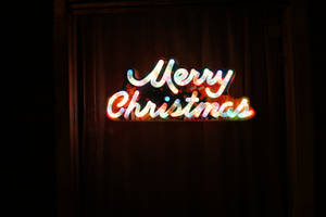 一個發光的霓虹燈牌在深色窗簾前顯示Merry Christmas。