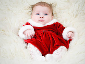 嬰兒穿著紅色天鵝絨聖誕老人服裝在柔軟的白色地毯上