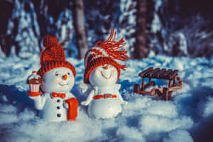 兩個戴紅帽的雪人公仔在雪地森林中拿著一個杯子蛋糕和一個雪橇。