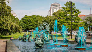 城市公園中的青銅噴泉和水柱，綠樹和建築。