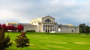 大型博物館建築，帶有柱子和雕像，位於長滿紅樹和散步人群的草坡上。