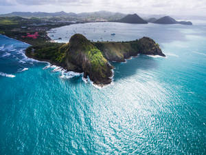 從高空俯瞰，碧綠的海浪拍打著綠色懸崖，遠處島嶼和沿海城鎮。 — 島嶼 壁紙
