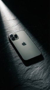 深色石板上的銀色iPhone，戲劇性聚光燈下，深邃陰影