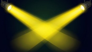 兩盞黃色舞台聚光燈在深色背景上交叉成X形。 — 電影 壁紙