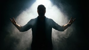 男人在煙霧黑暗中於聚光燈下伸展雙臂的剪影。