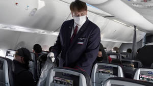 空中服務員戴口罩在美國航空公司飛機上為乘客服務。