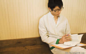戴眼鏡的年輕男子在室內木長椅上閱讀。