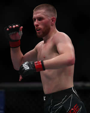 一位赤裸上身的男性MMA拳手，在八角籠內戴著黑色和紅色手套。