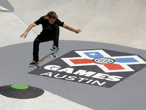 滑板手在混凝土坡道上的X Games Austin標誌上方表演技巧。