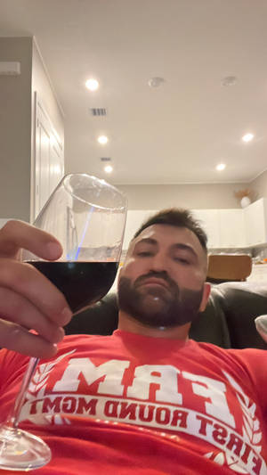 著紅色衫嘅男人喺室內拎住一杯紅酒放鬆。