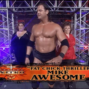 摔角手 Mike Awesome 在擂台上，身後有兩名女子，在舞台燈光下。